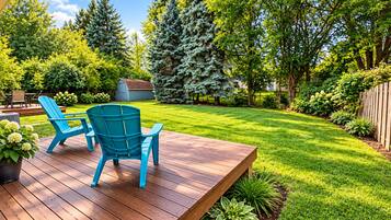 A deck with two chairs and a table, surrounded by a well-maintained lawn and various trees.