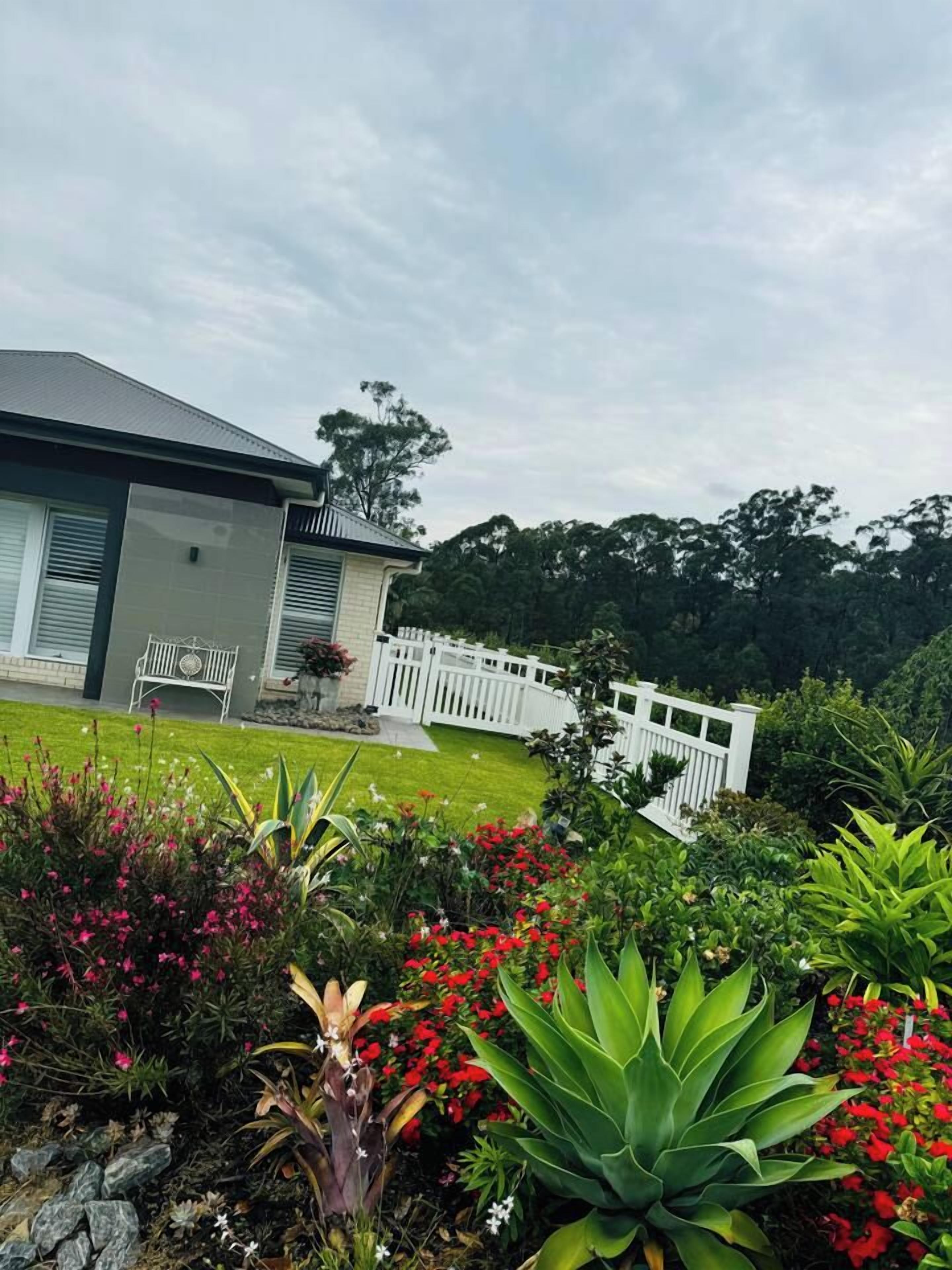 Una casa con un cerco blanco, un césped y diversas plantas.