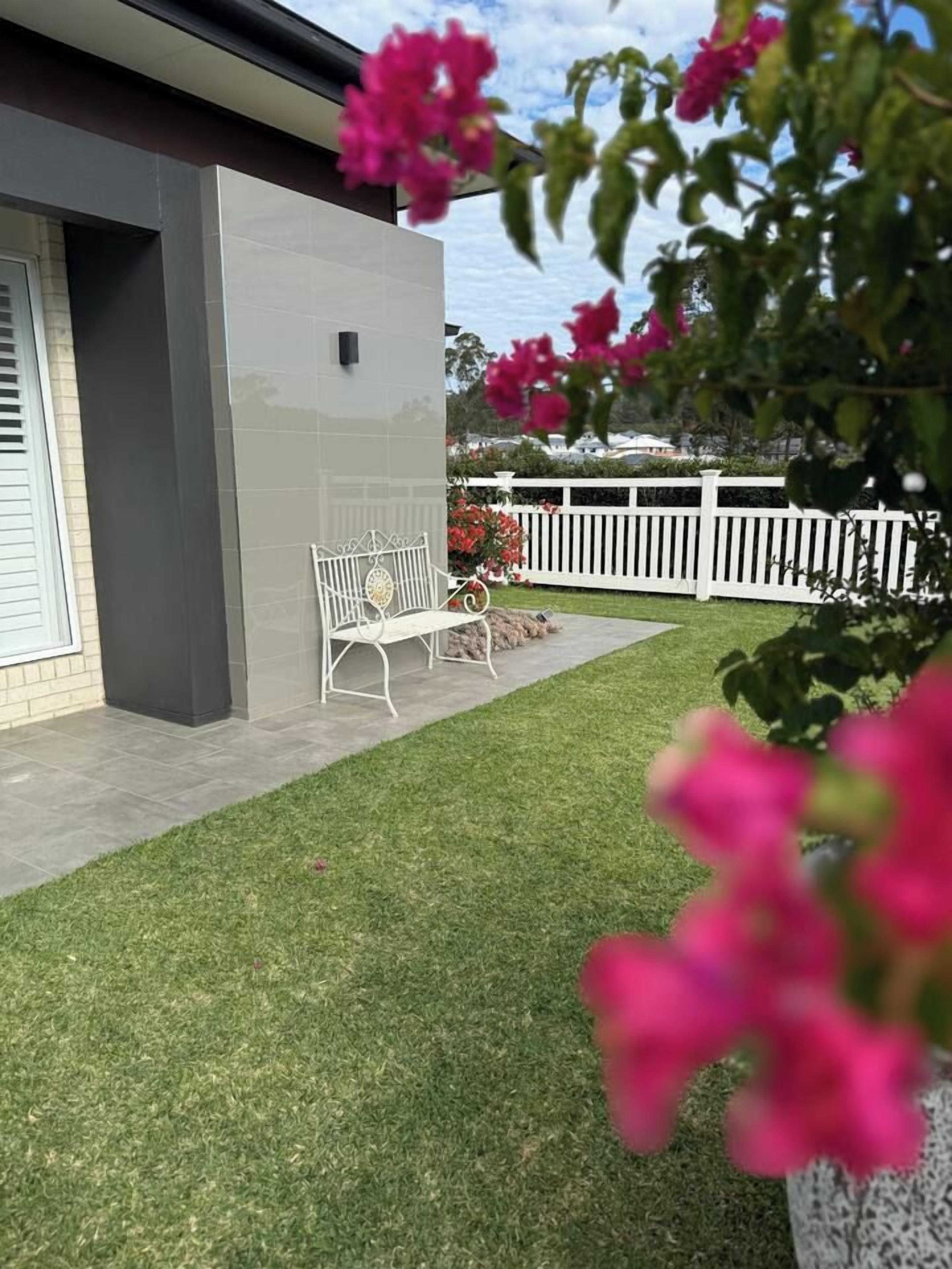 A modern building with a grey exterior, a white fence, a bench, and a well-maintained lawn.