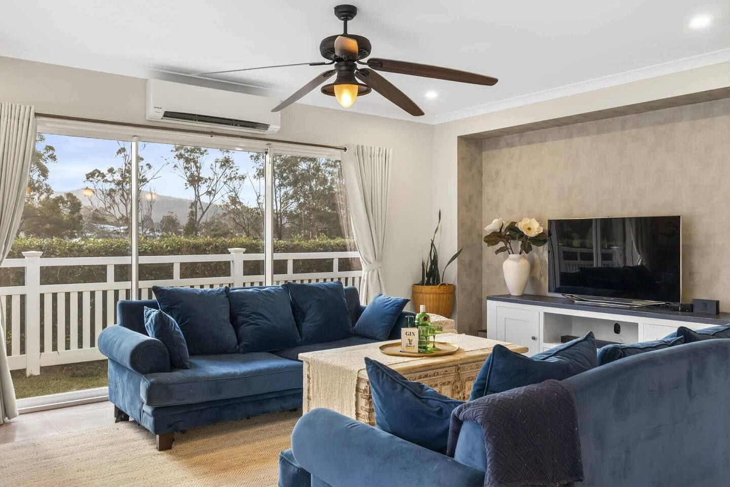 Una sala de estar con un sofá modular, una mesa de centro, un televisor y un ventilador de techo.