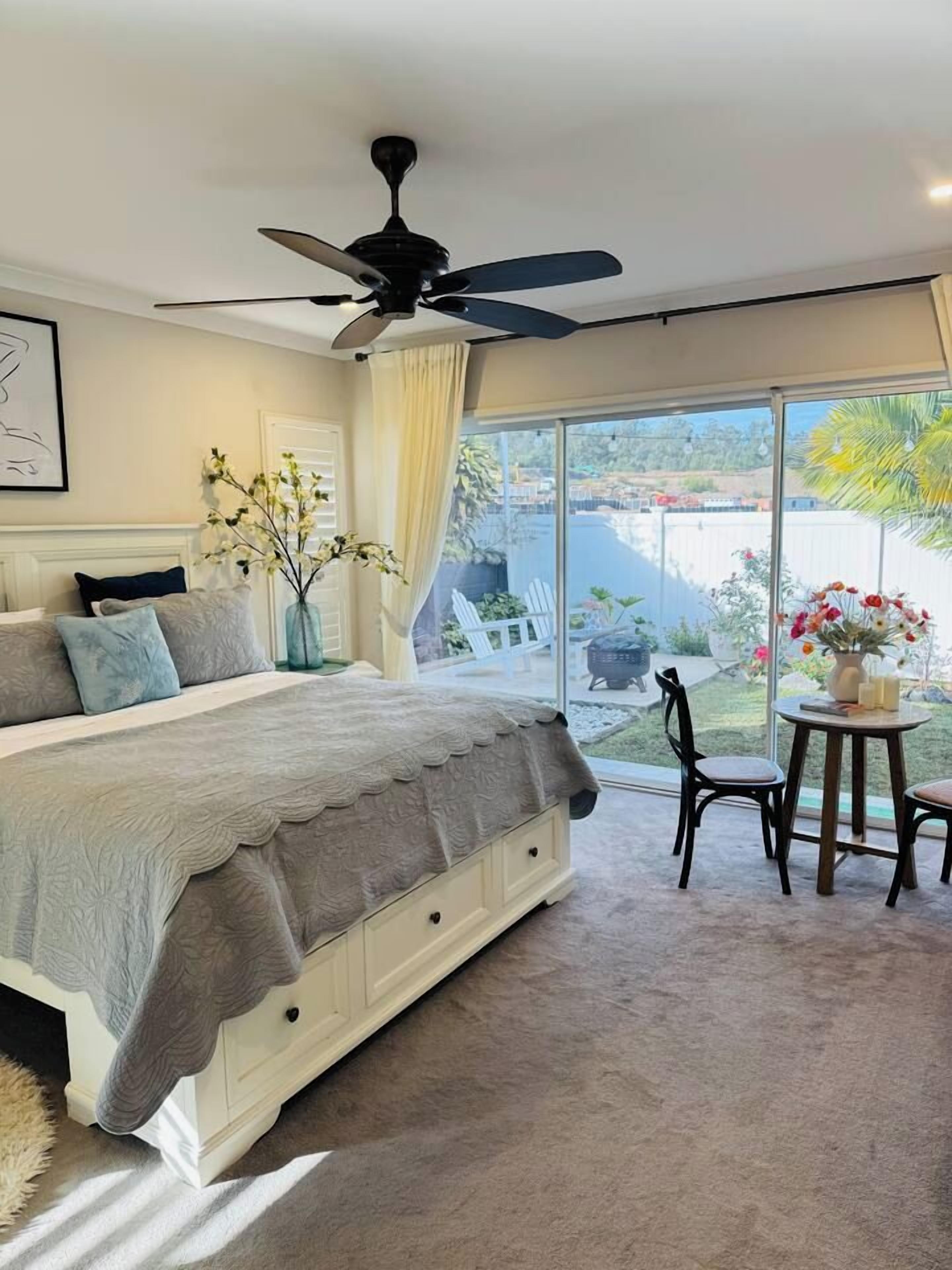 A bedroom with a large bed, a ceiling fan, and a view of the outdoors.