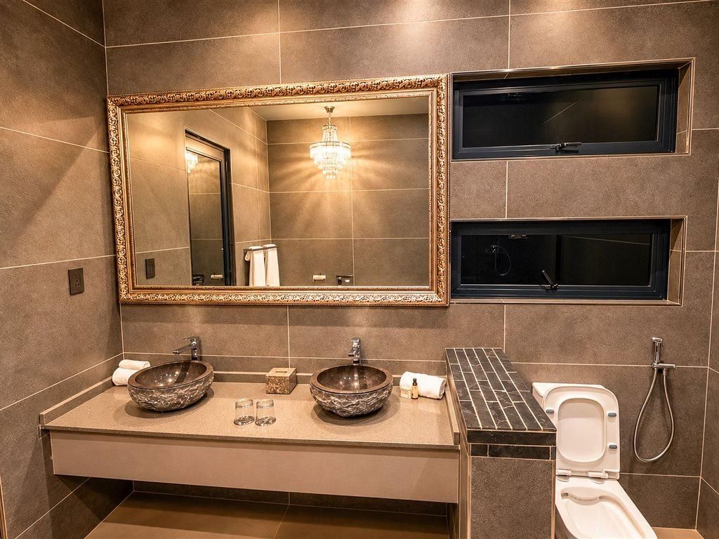 A modern bathroom with a double sink, a large mirror, and a toilet with a shower attachment.