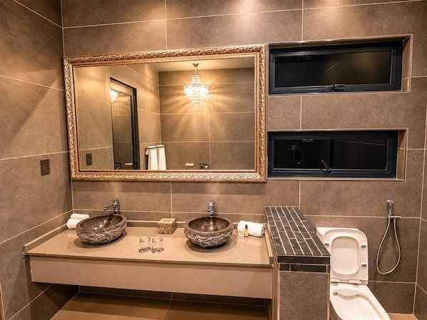 A modern bathroom with a double sink, a large mirror, and a toilet with a shower attachment.