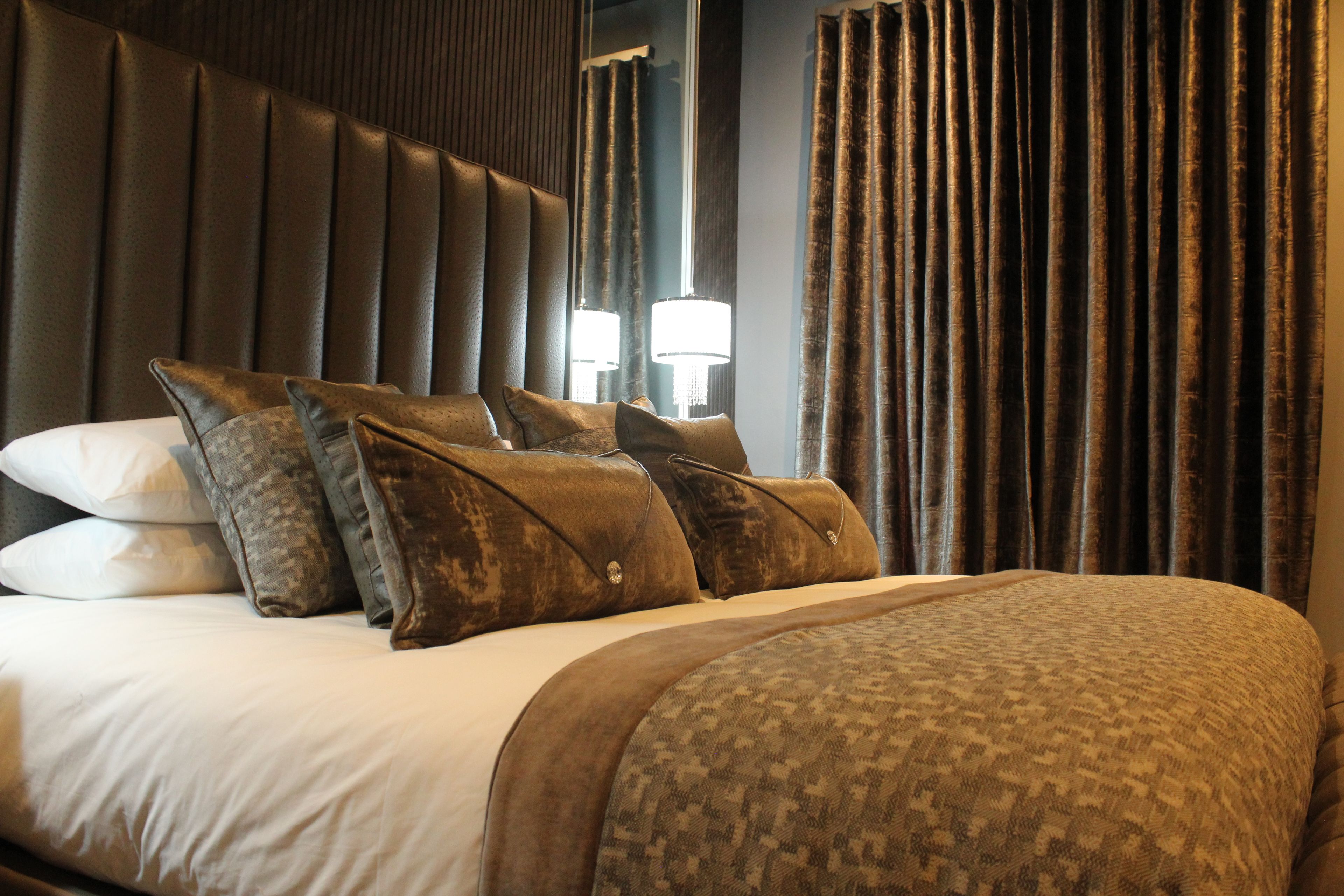 Una habitación de hotel con una cama grande, varias almohadas, un cabecero y cortinas.