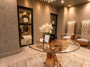 A hotel lobby with a round glass table, two chairs, and a mirror with a number sign.