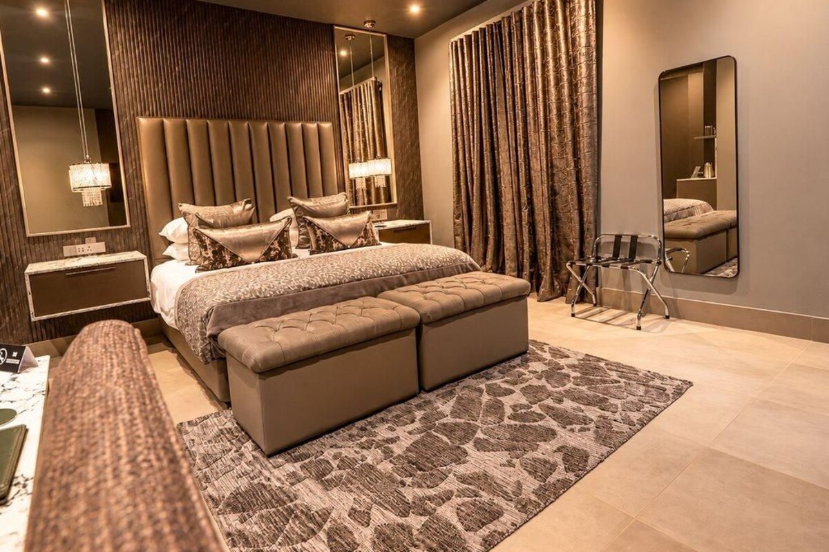 A modern bedroom with a large bed, a bedside table, a mirror, and a curtain.