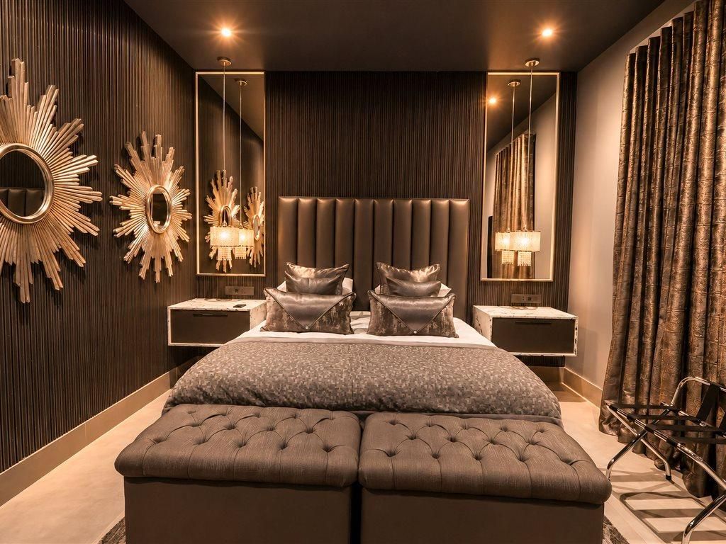 Un dormitorio moderno con una cama grande, dos mesitas de noche, un espejo y un banco tapizado.