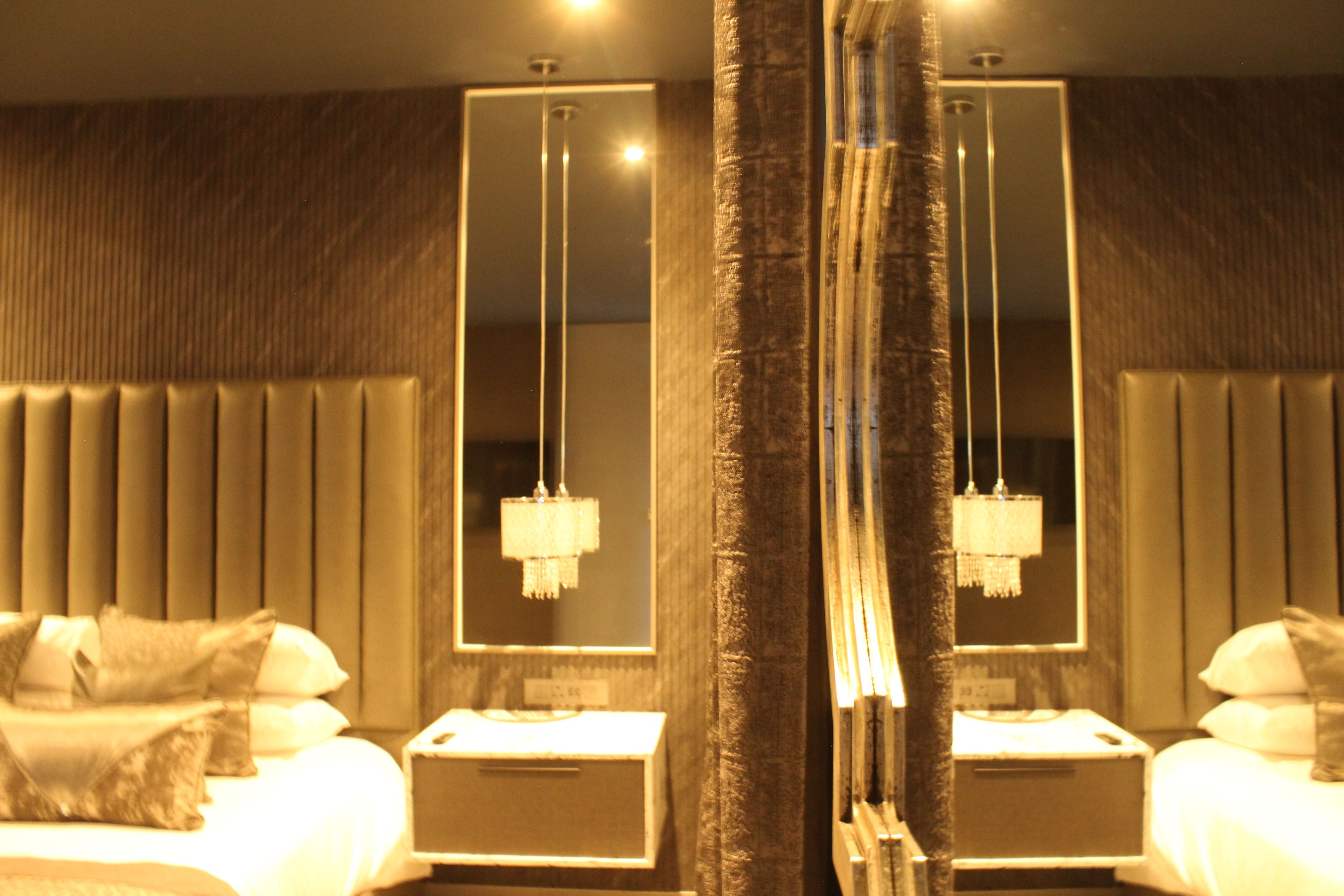 A hotel room with a large bed, a nightstand, a mirror, and a chandelier.
