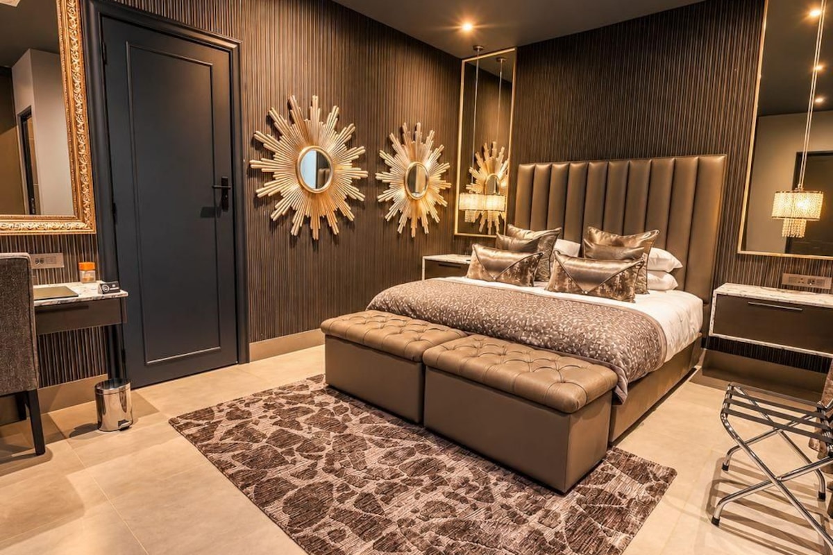 A modern bedroom with a large bed, a chest of drawers, a vanity, and decorative mirrors.