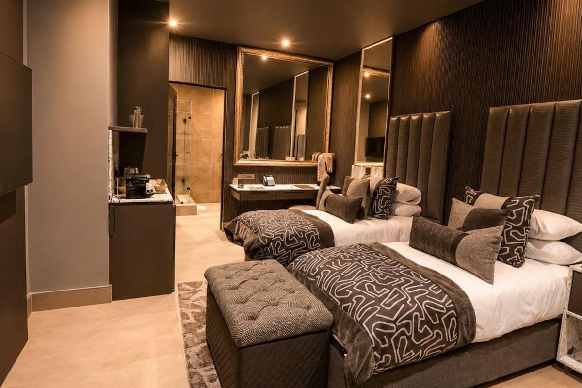 A modern bedroom with two beds, a large mirror, and a vanity with a sink.