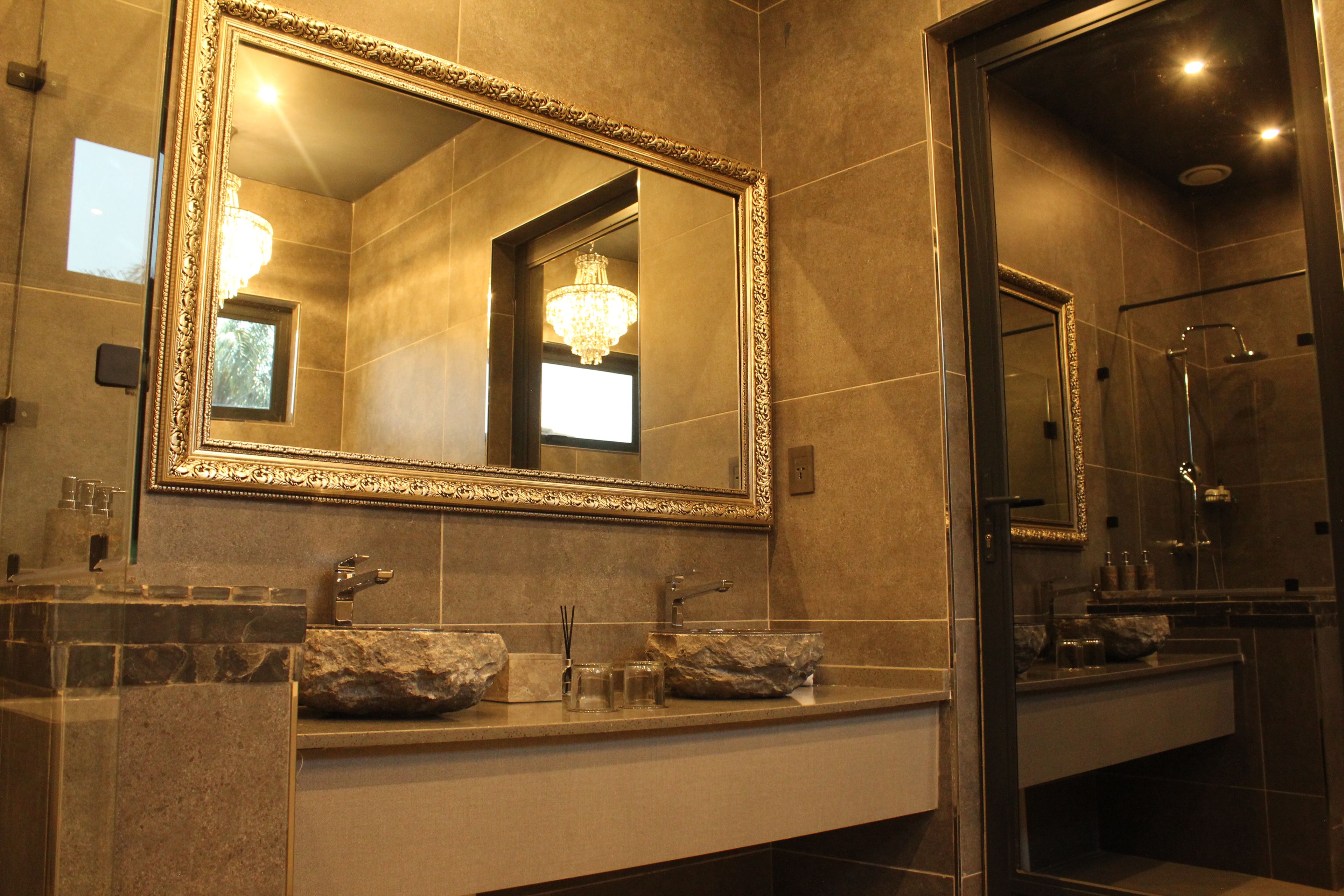 A bathroom with a large ornate mirror, a chandelier, and a modern shower.