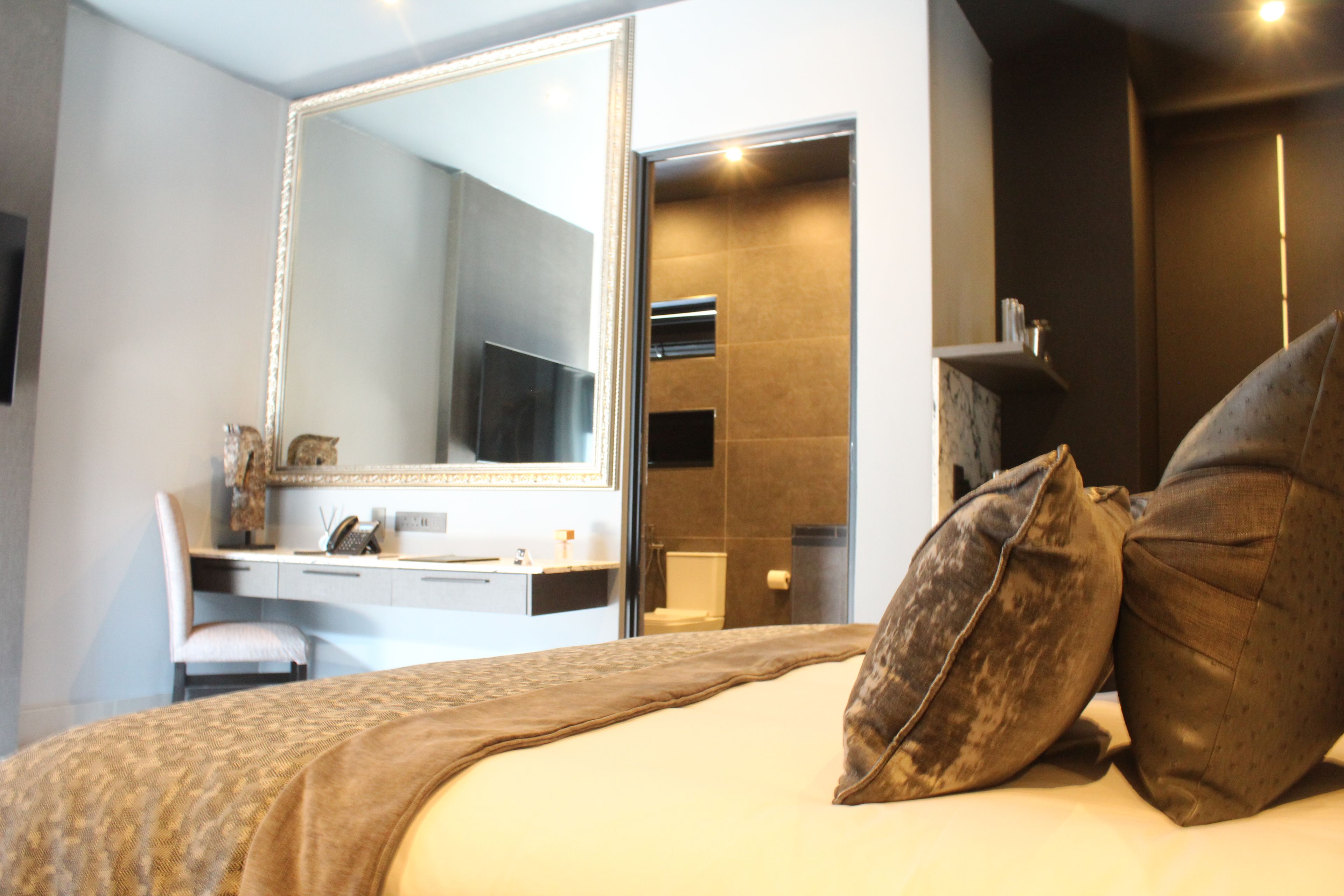 Une chambre d’hôtel moderne, dotée d’un grand lit, d’un bureau, d’un miroir et d’une salle de bain visible à travers une porte ouverte.