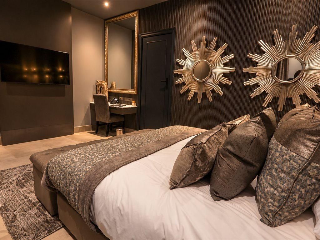 A modern bedroom with a large bed, a bedside table, a mirror, and a wall-mounted sunburst mirror.