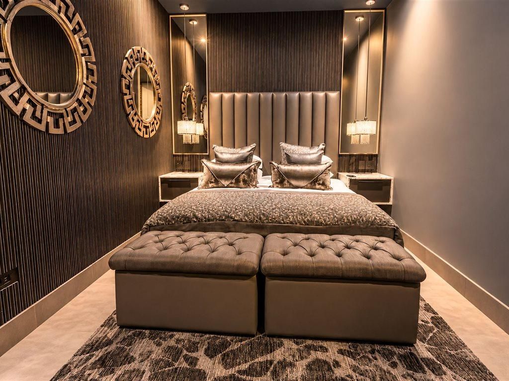 Un dormitorio con una cama grande, dos sillones, un cabecero y lámparas de pared.