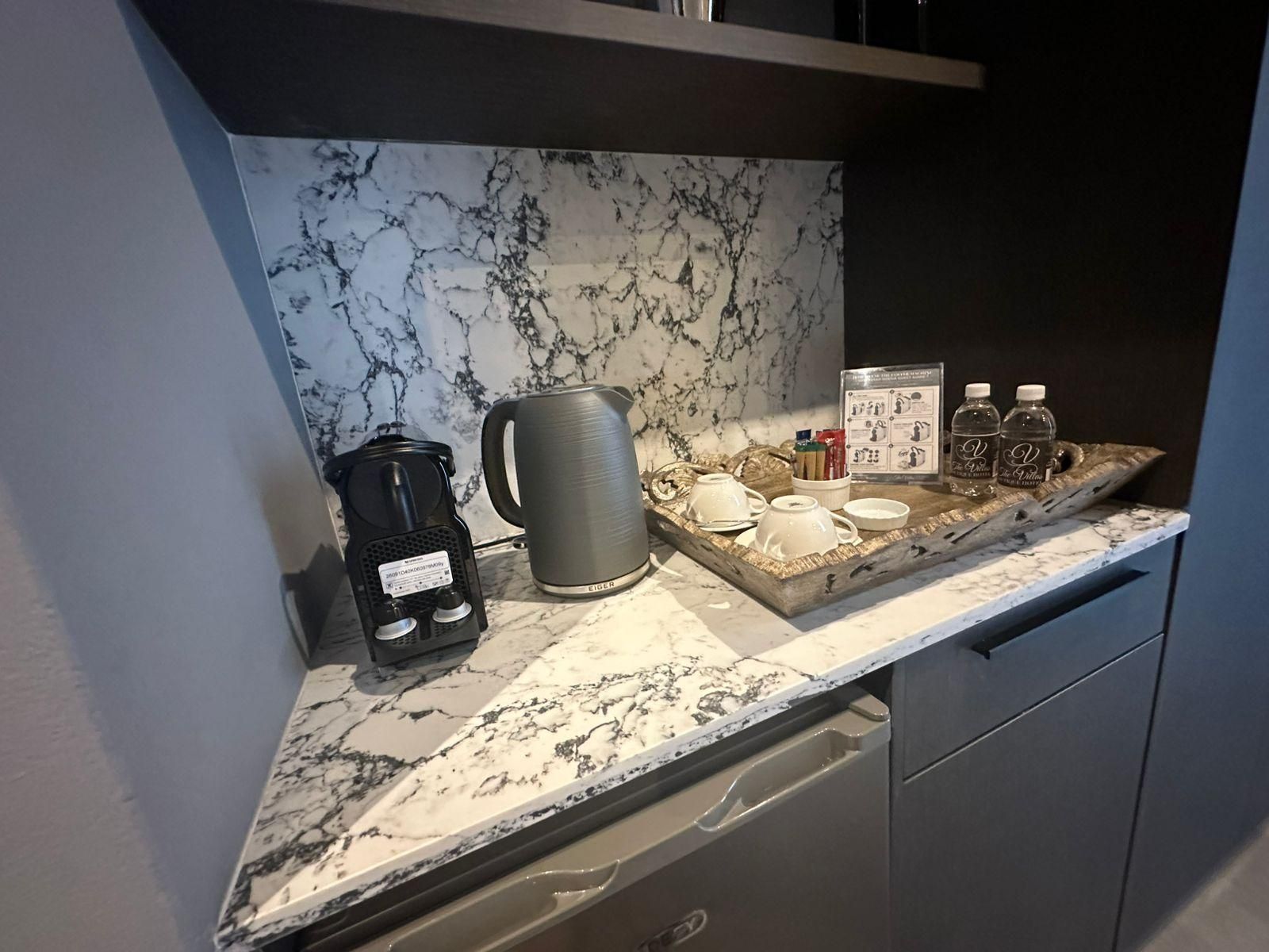 Una encimera de cocina con cafetera, hervidor y una bandeja con tazas y condimentos.