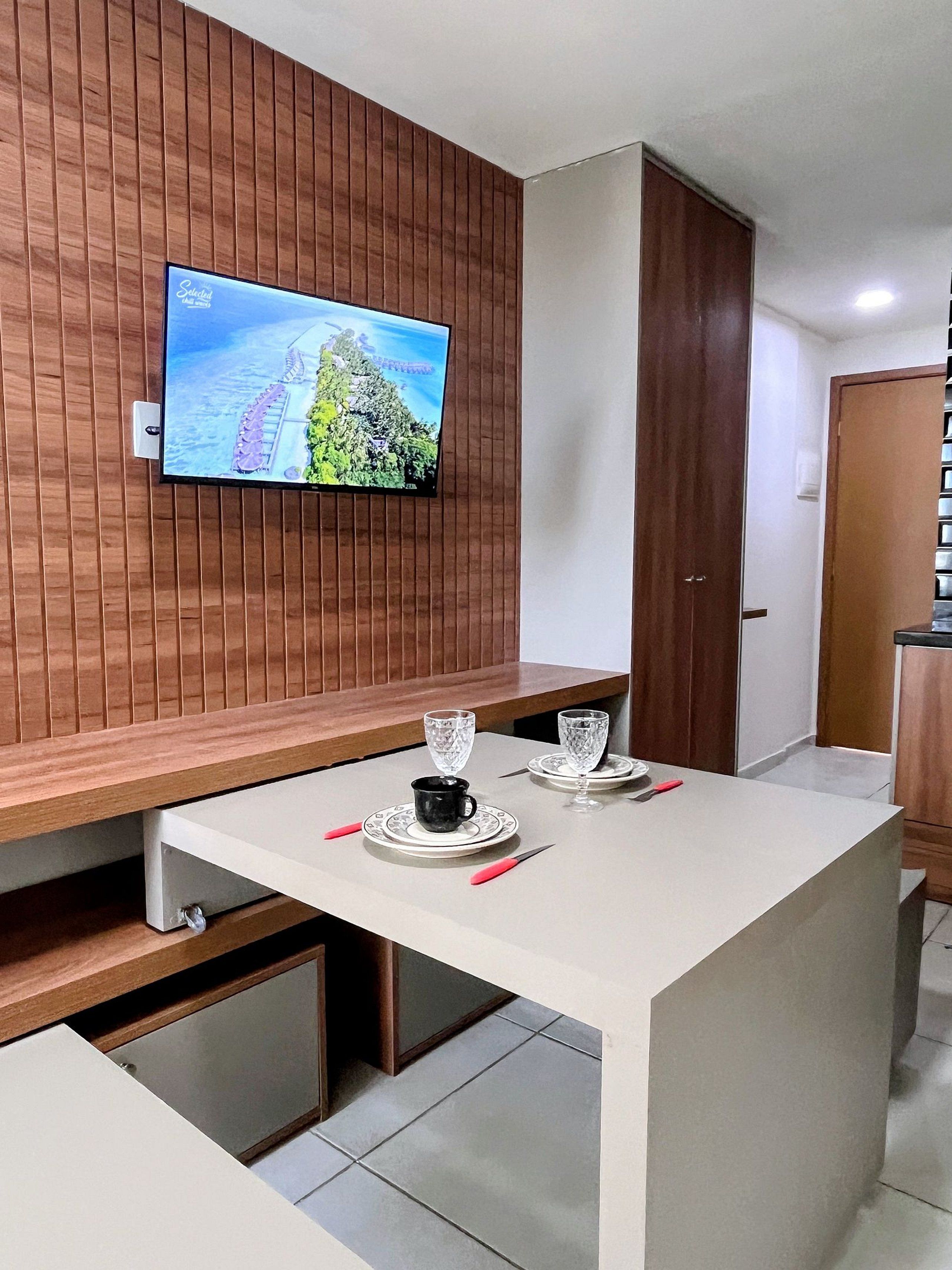 Een moderne keuken met een ingebouwde televisie waarop een mooi landschap te zien is, een eettafel met een zwarte mok en twee wijnglazen, en houten wandbekleding.