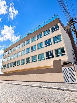 Ein mehrstöckiges Gebäude mit schlichter Fassade, großen Fenstern und einem Balkon im oberen Stockwerk.