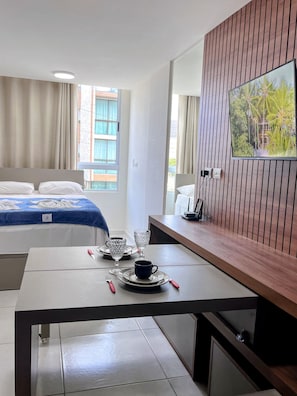 A hotel room with a bed, a dining table with cutlery, a television, and a window with curtains. - Eco Mirage - VSH (Ipojuca)