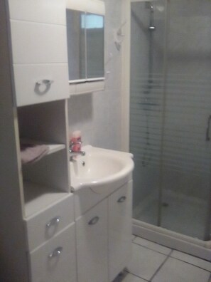 Een badkamer met een wit wastafelmeubel, spiegel en een douchecabine van glas.