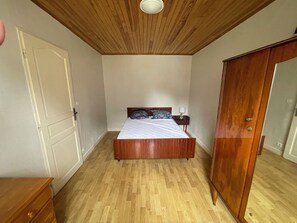 Een slaapkamer met een houten bed, een kledingkast, een nachtkastje met een lamp en een deur.