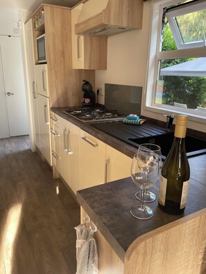 A modern kitchen with a built-in stove, a coffee maker, and a wine bottle on the counter. - Chalet Toetje op de Veluwe Hoenderloo (Hoenderloo)