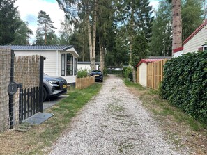 A gravel path leading to a row of mobile homes with a fenced area on one side and a hedge on the other. - Chalet Toetje op de Veluwe Hoenderloo (Hoenderloo)
