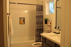 Un baño con ducha de azulejos blancos, inodoro y lavabo con espejo.