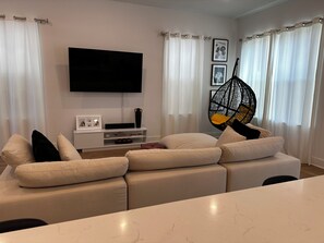 Una sala de estar con sofá, televisor de pantalla plana, sillón colgante y mesa de comedor.