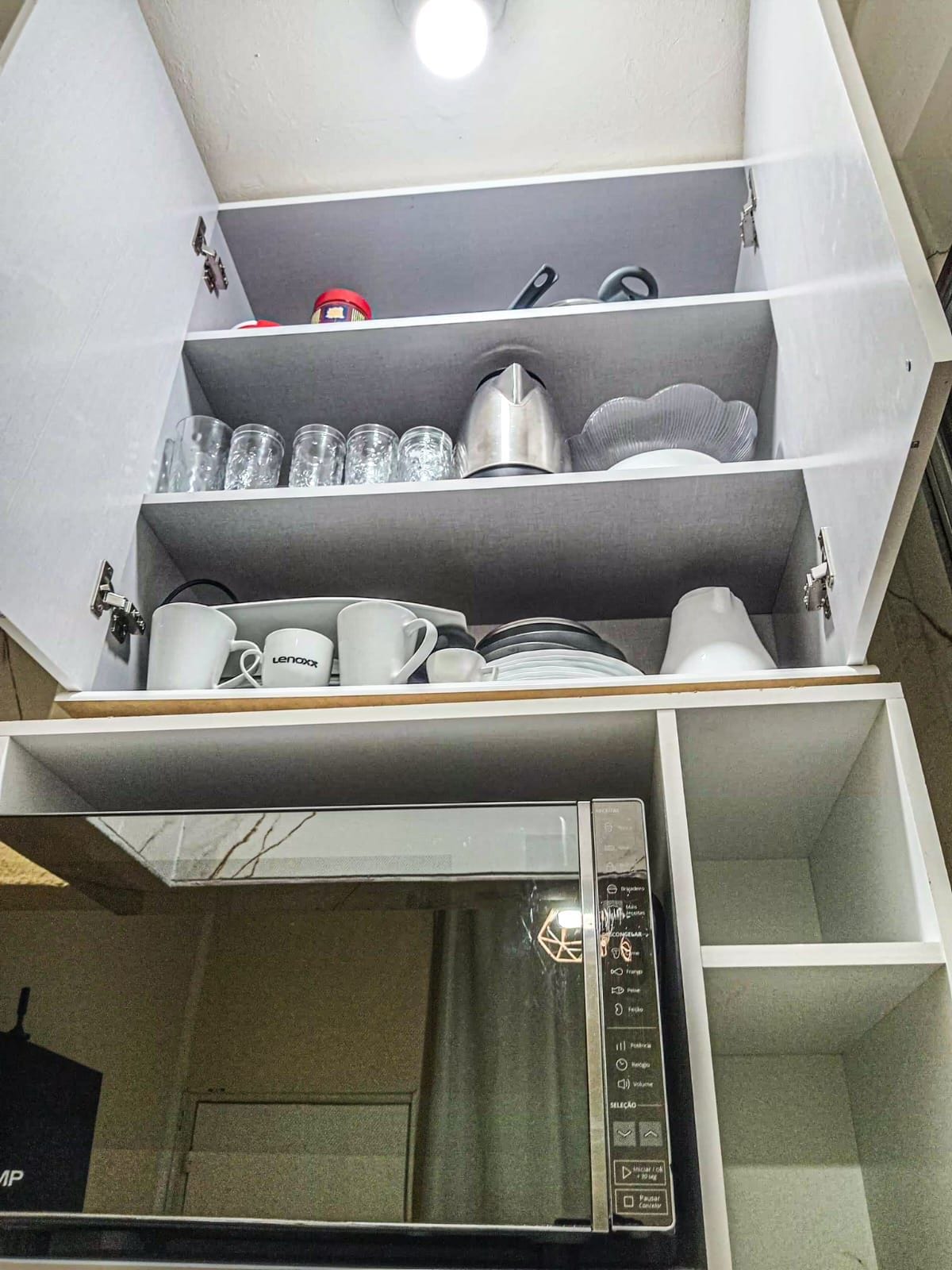 Una cocina con microondas, cafetera y un estante con diversos utensilios de cocina.