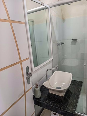 Un bany amb box de dutxa de vidre, un lavabo blanc i una superfície de marbre.
