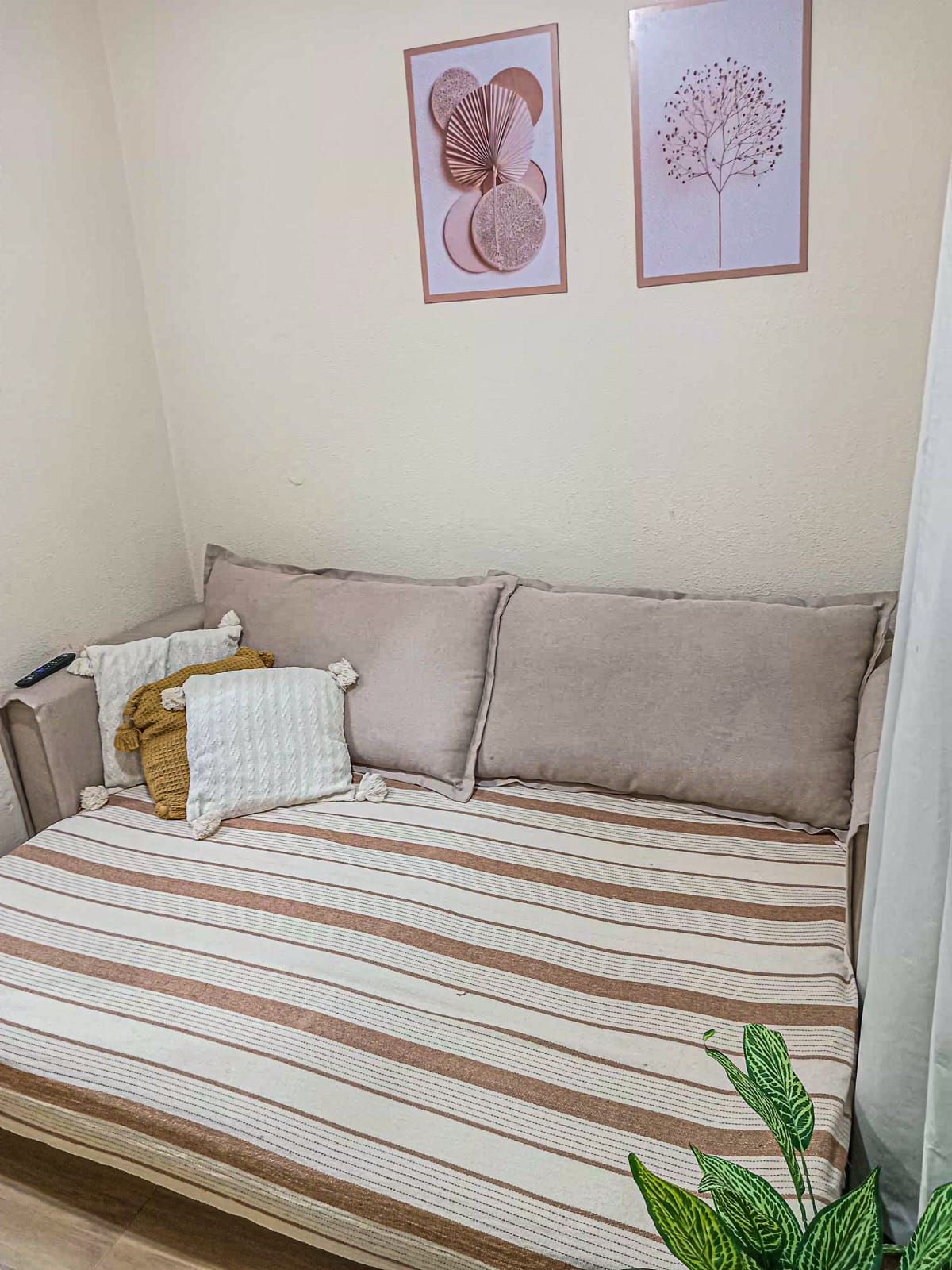 A room with a sofa bed, a blanket, pillows, a remote control, and two framed pictures on the wall.