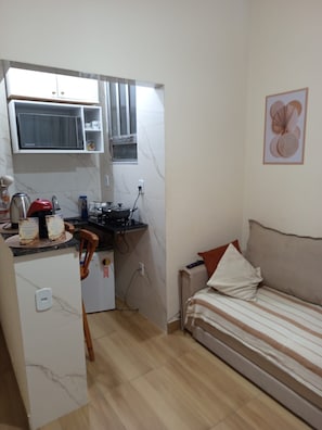 Un espai habitable petit amb una cuineta, un llit i una obra d'art penjada a la paret.