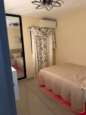A bedroom with a bed, an air conditioning unit, a ceiling fan, and a door leading to another room. - 3-bedroom apartment in fantastic Santo Domingo Este with AC and gym (Santo Domingo Este)