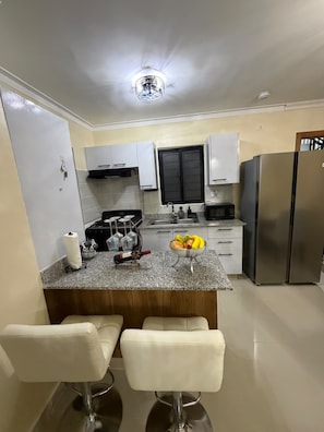 A modern kitchen with a central island, two bar stools, a stainless steel refrigerator, and a black cabinet above the sink. - 3-bedroom apartment in fantastic Santo Domingo Este with AC and gym (Santo Domingo Este)
