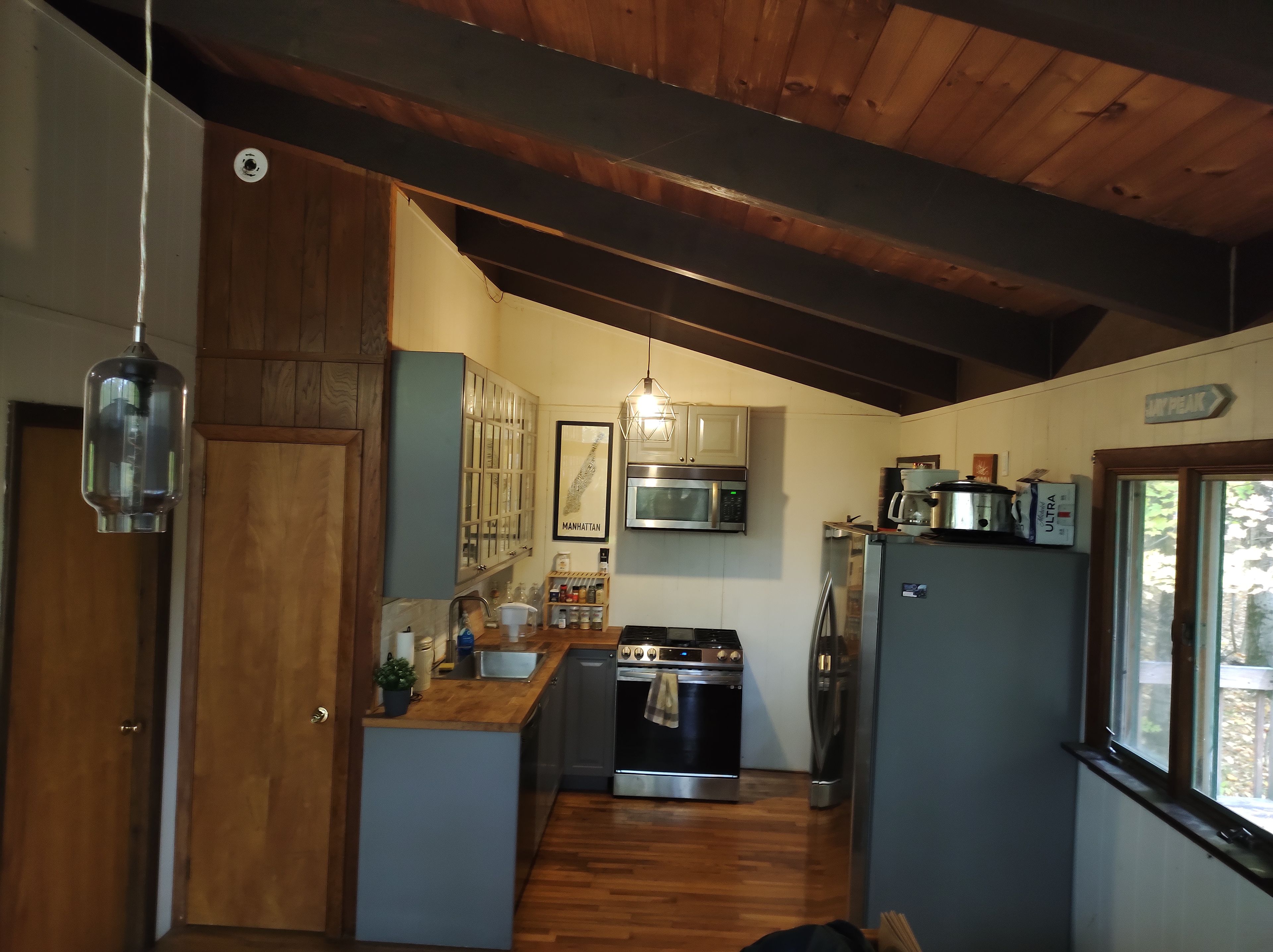 A compact kitchen with wooden beams, a stainless steel refrigerator, a microwave, an oven, and a sink.