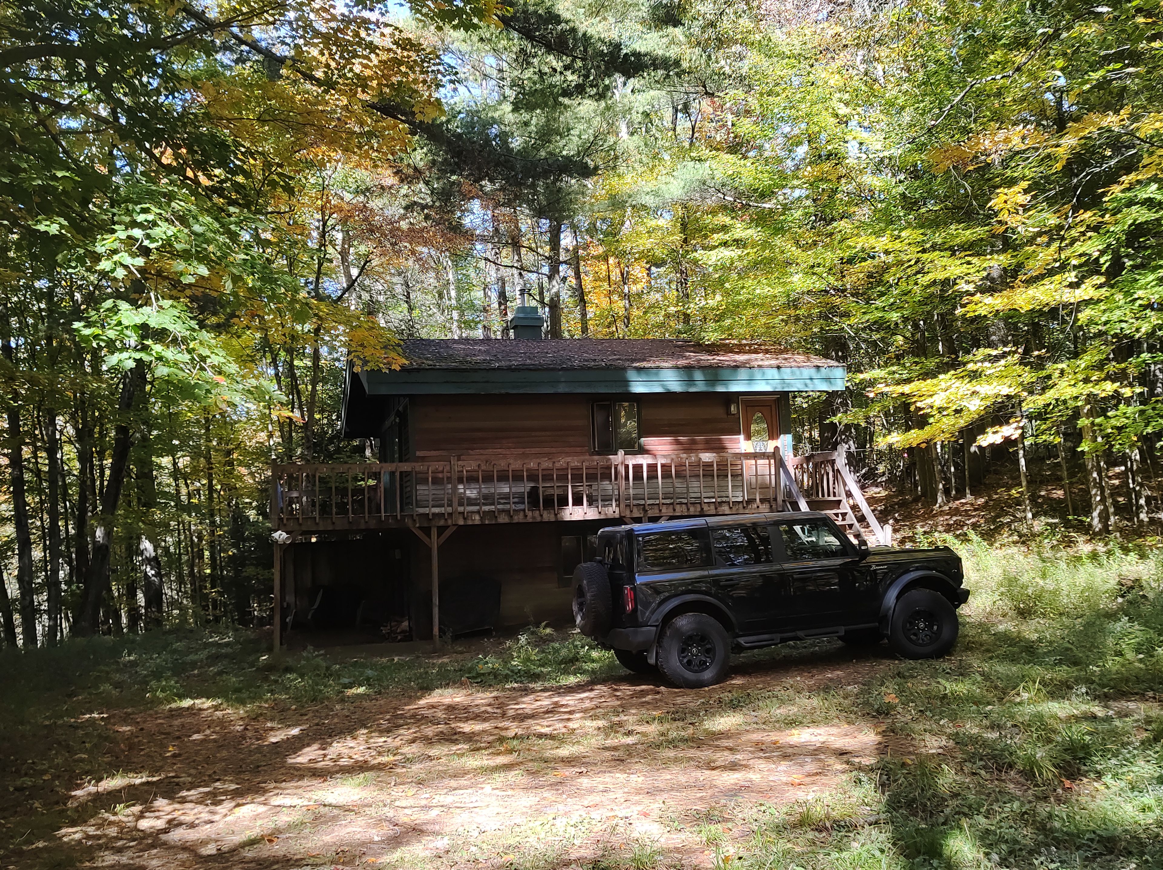 A cabin with a wooden deck and a vehicle parked in front.