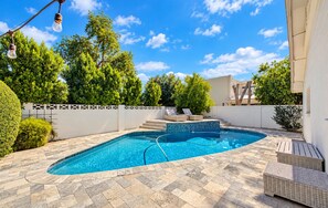 Une piscine avec une terrasse carrelée, entourée d’une clôture blanche, et un ciel bleu dégagé au-dessus.