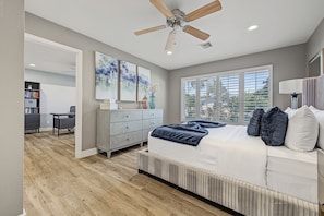 Une chambre à coucher avec un lit, un ventilateur de plafond et une vue sur l’extérieur grâce à de grandes fenêtres.