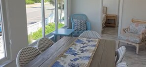 Una habitació amb taula de menjador, dues cadires de vimetla, un relaxant blau i un sofà amb coixins estampats.