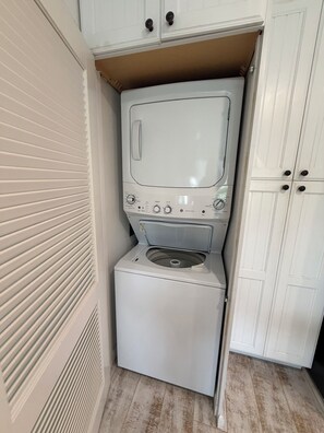 A compact laundry room with a washing machine and dryer, white cabinetry, and a vented wall. - GulfDrift— Beachfront Boca Grande — On the Gulf (Boca Grande)