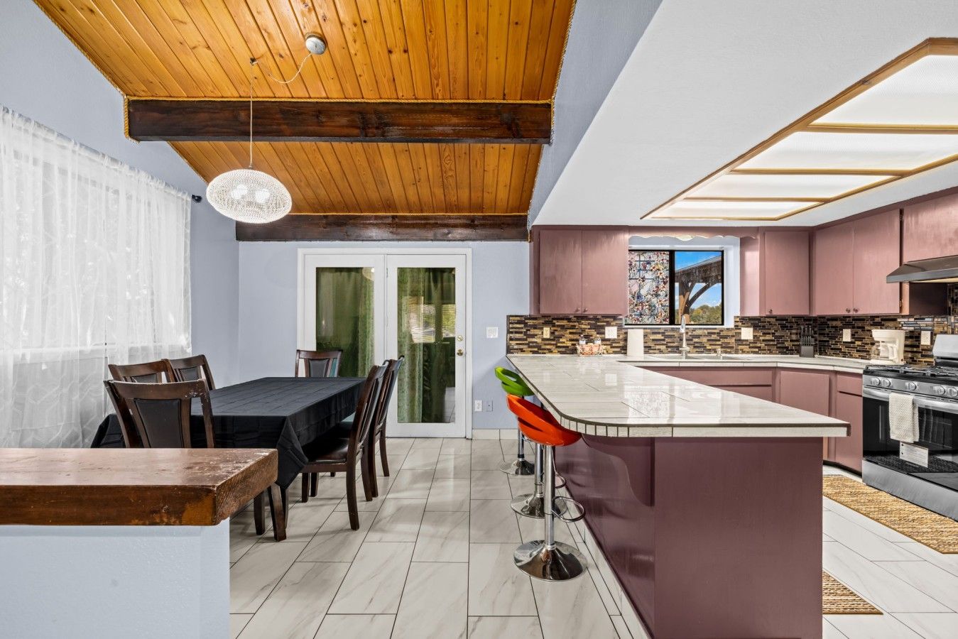 A modern kitchen with a central island, wooden ceiling, and a dining area with chairs.