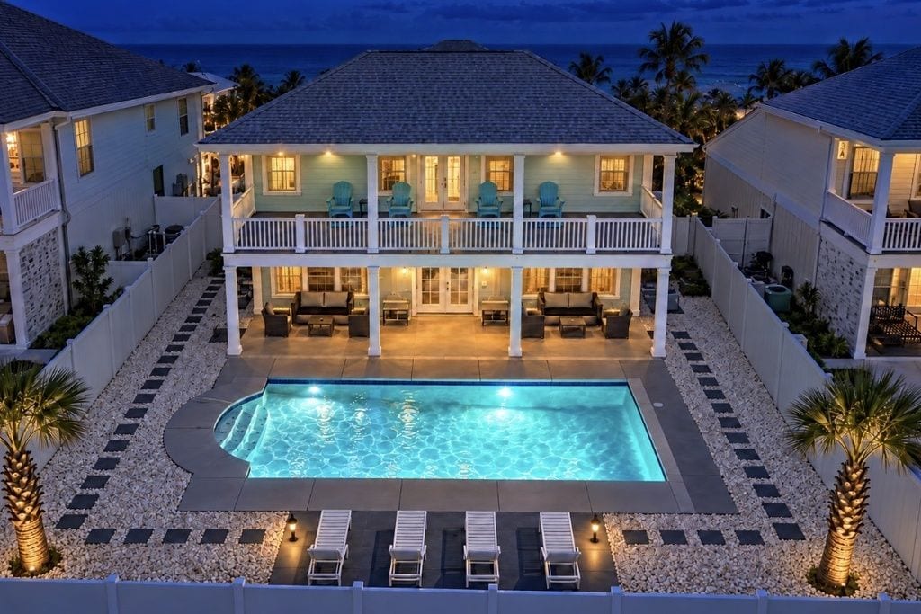 Una casa de dos pisos con piscina, mobiliario exterior y vista al océano.