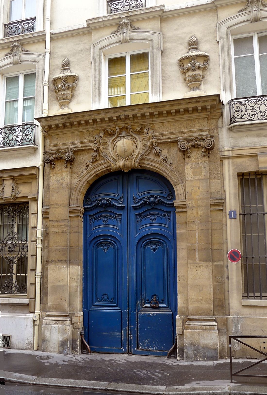 A building facade with a large blue double door, ornate architectural details, and a barred window.