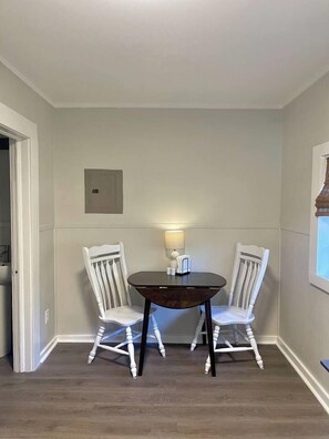 A dining area with a round table and two white chairs, a wall-mounted light, and a window with blinds. - Second Floor Studio | 0.3 Miles from SFA (Nacogdoches)
