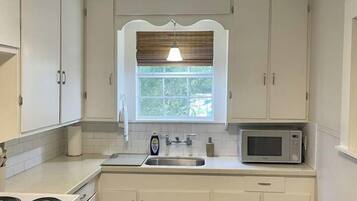 A compact kitchen with white cabinets, a microwave, a stove, and a window with blinds.