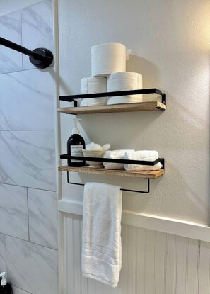 Ein Badezimmer mit Handtuchhalter, Handtuch, Ablagen für Toilettenartikel und Toilettenpapierhalter.