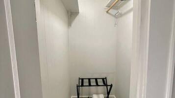 A narrow hallway with white walls and a door on the left. A black rack with folded items is placed against the wall.