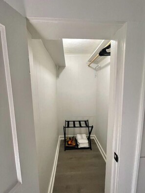 A narrow hallway with white walls and a door on the left. A black rack with folded items is placed against the wall. - Second Floor Studio | 0.3 Miles from SFA (Nacogdoches)