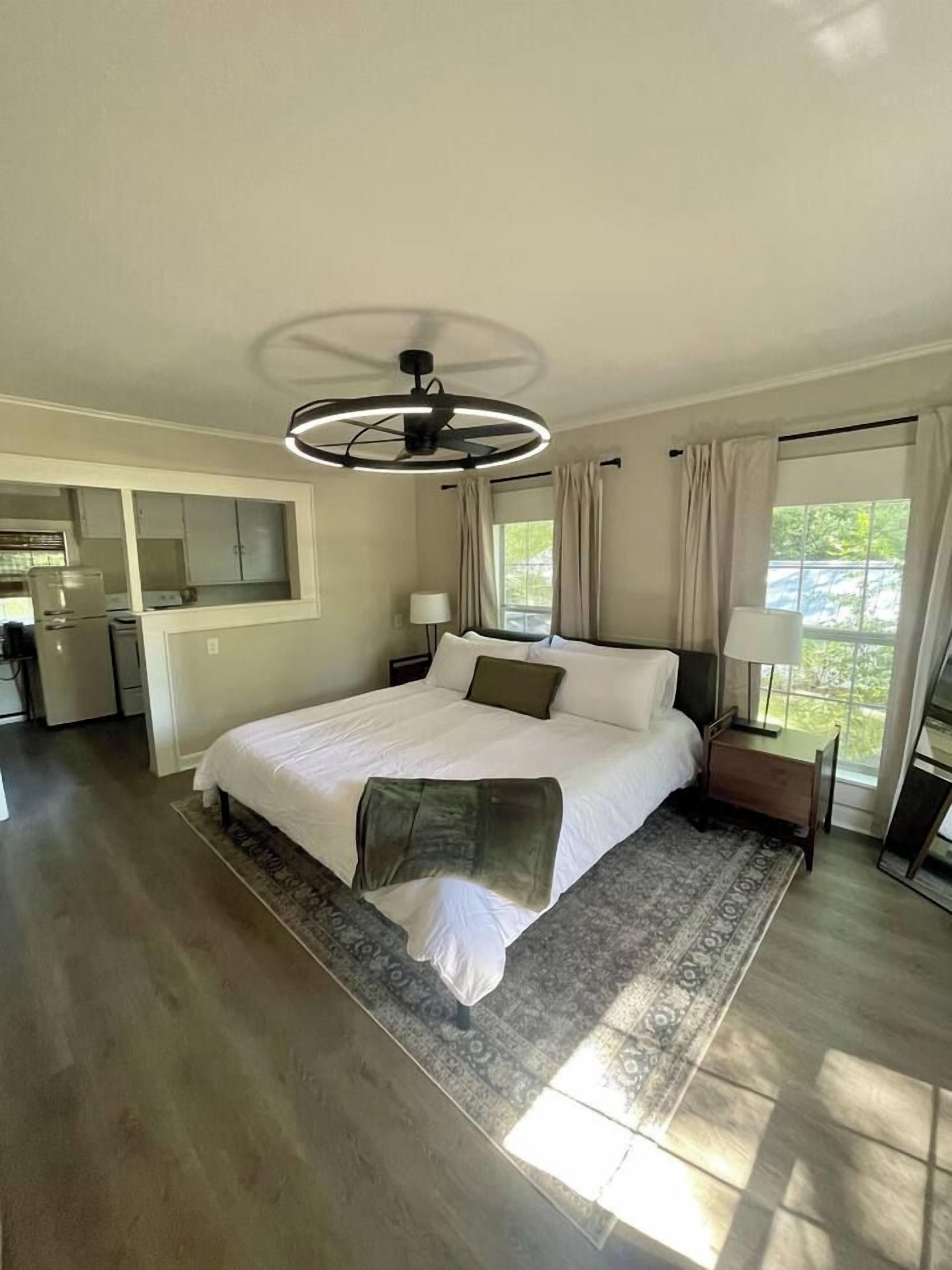 A bedroom with a bed, bedside tables, a ceiling fan, and a view of the outdoors.