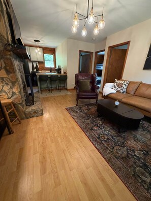 Ein Wohnzimmer mit Kamin aus Stein, Holzböden, einem Ledersessel, einer Couch und einem Couchtisch.